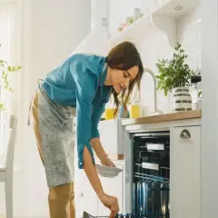 Kobieta wkłada talerz do zmywarki. Zastanawia się, czy lepsza będzie zmywarka 45 czy 60 cm.