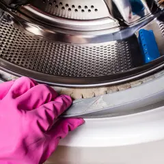 Rękawica w różowym kolorze pokazuje, jak odgrzybić pralkę, czyszcząc uszczelkę bębna z nalotu.