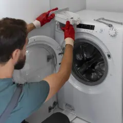 Serwisant w czerwonych rękawiczkach wyjmuje szufladę na proszek z pralki z wymiennymi łożyskami.