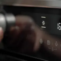 Dłoń obraca pokrętło piekarnika Whirlpool, wybierając funkcje oznaczone symbolami. Na wyświetlaczu 160°C.