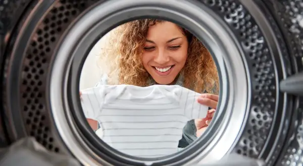 Uśmiechnięta kobieta wkłada ubranko do suszarki bębnowej Whirlpool.