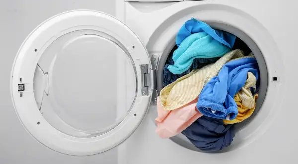 Pralka nie wiruje tylko buczy, a w środku kolorowe pranie. Drzwiczki otwarte, widać ubrania.