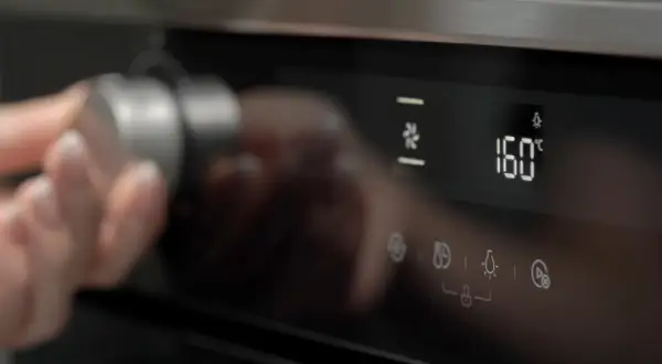 Dłoń obraca pokrętło piekarnika Whirlpool, wybierając funkcje oznaczone symbolami. Na wyświetlaczu 160°C.