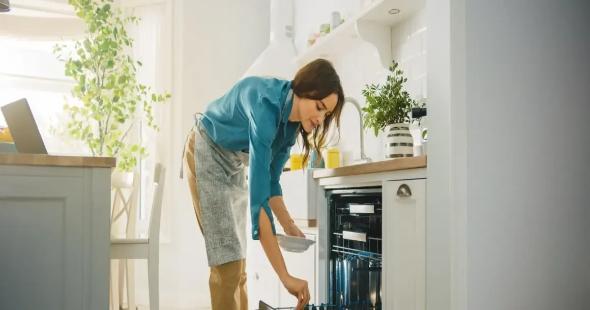 Kobieta wkłada talerz do zmywarki. Zastanawia się, czy lepsza będzie zmywarka 45 czy 60 cm.