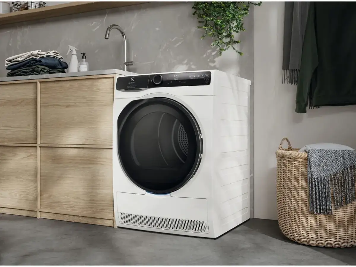 Nowoczesna, biała suszarka do ubrań Electrolux w łazience. Obok kosz z kocem i wiszące ubrania.